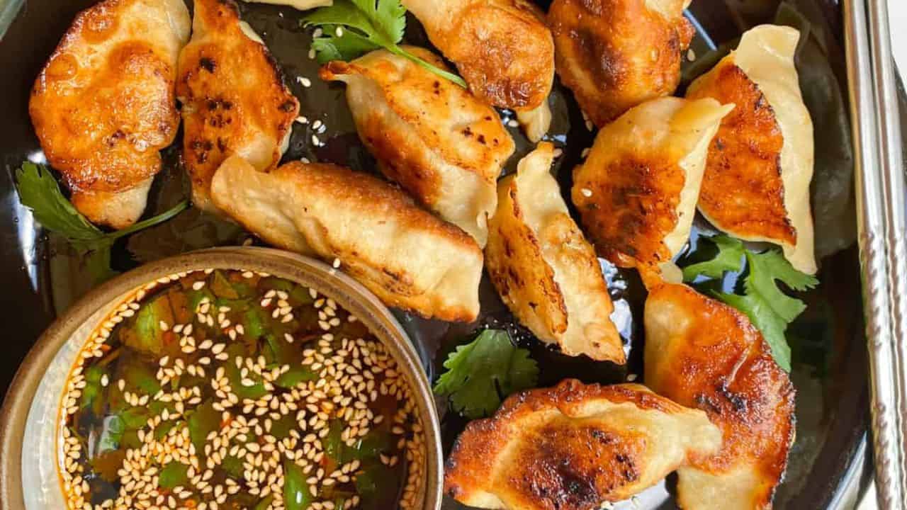 Crispy-bottom pan-fried dumplings with juicy and savory fillings on a black plate with a sauce on the side.