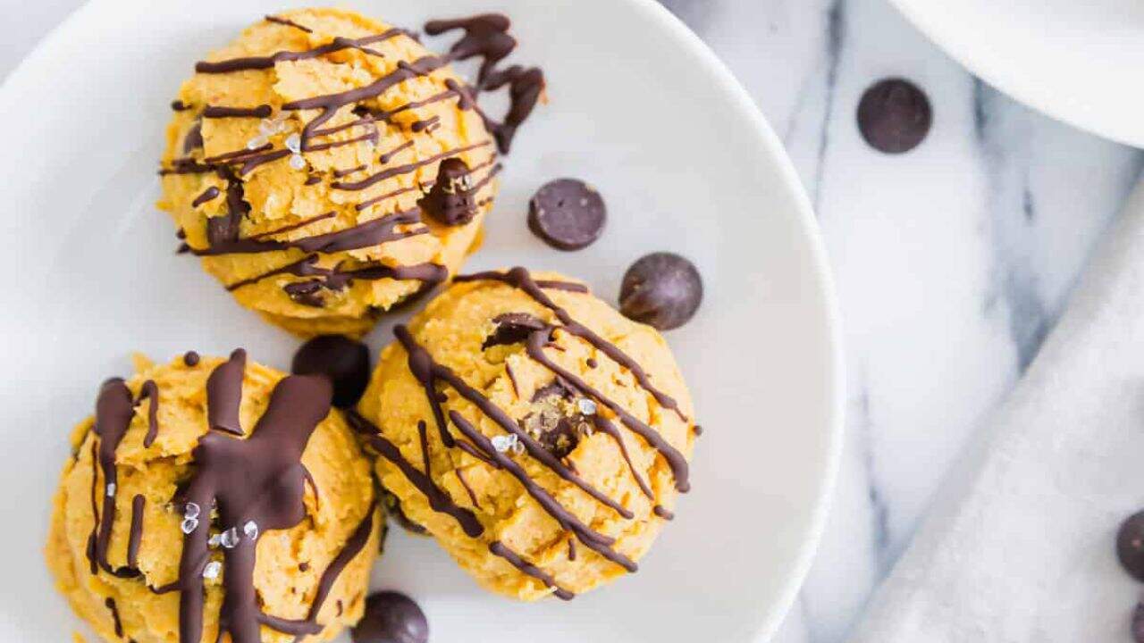 Pumpkin cookie dough bites on a white surface drizzled in chocolate.
