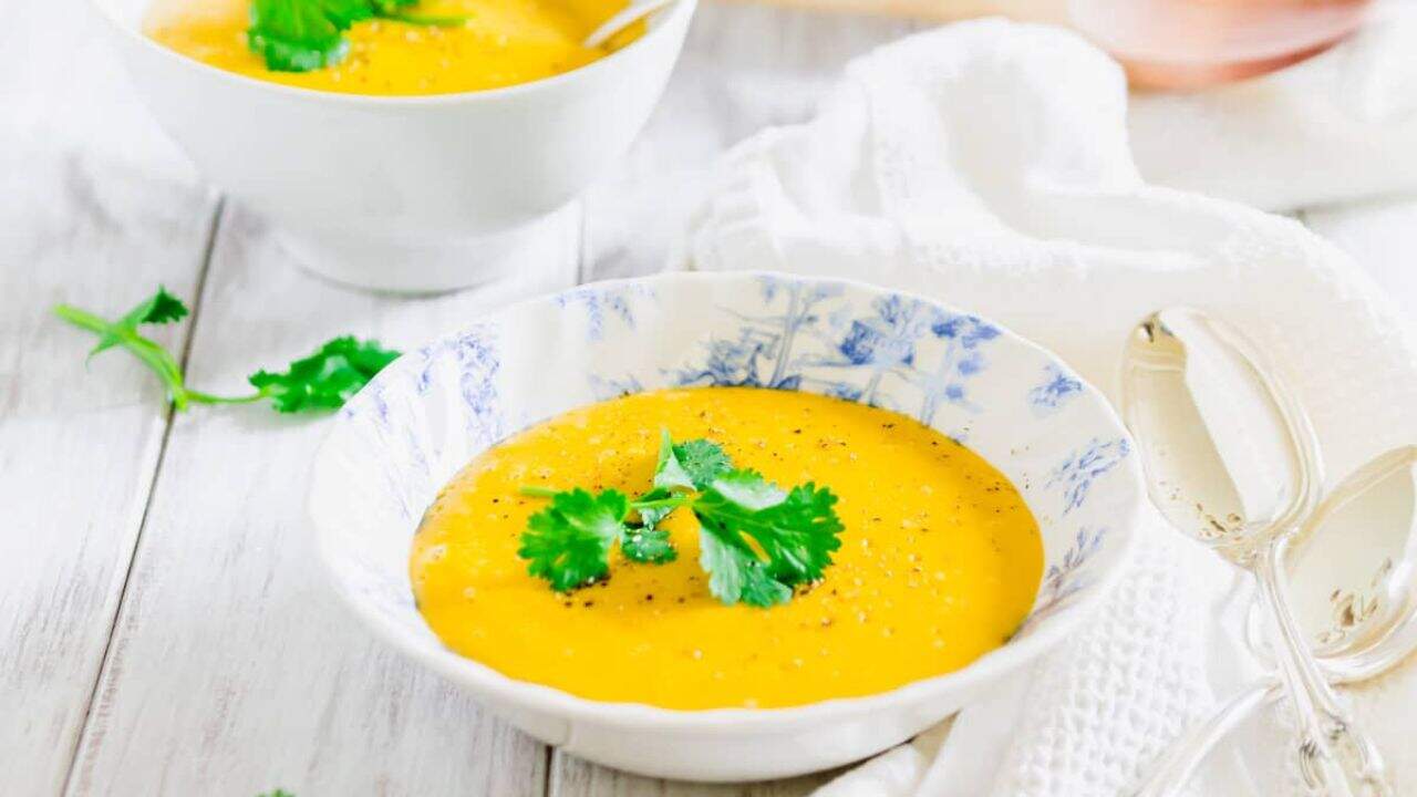 Pumpkin potato blender soup in a blue and white bowl garnished with fresh parsley.