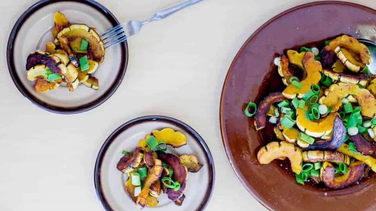 Roasted squash with scallions on a brown plate.