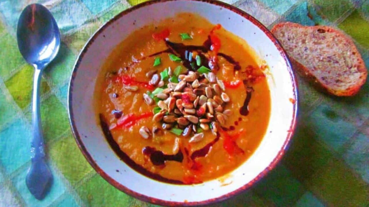 A bowl of soup garnished with seeds, chopped herbs, and drizzles of sauce.