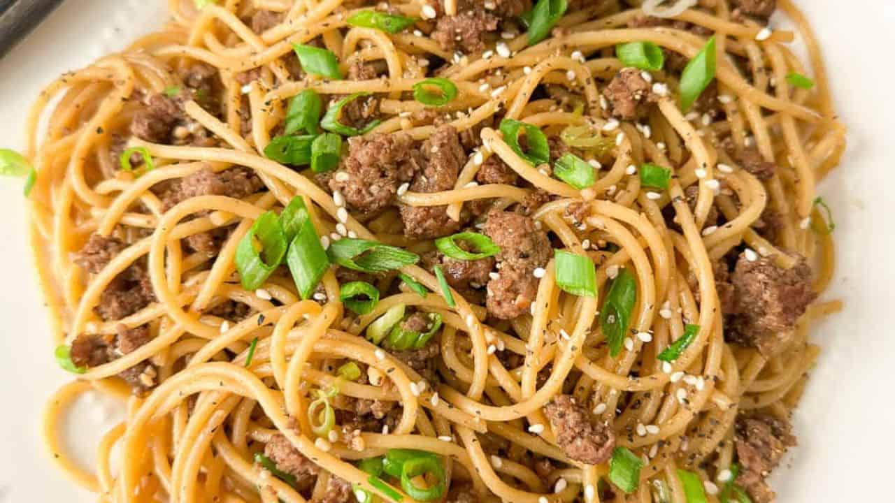 A plate of Chinese Mongolian beef noodles garnished with fresh green onions and roasted sesame seeds.