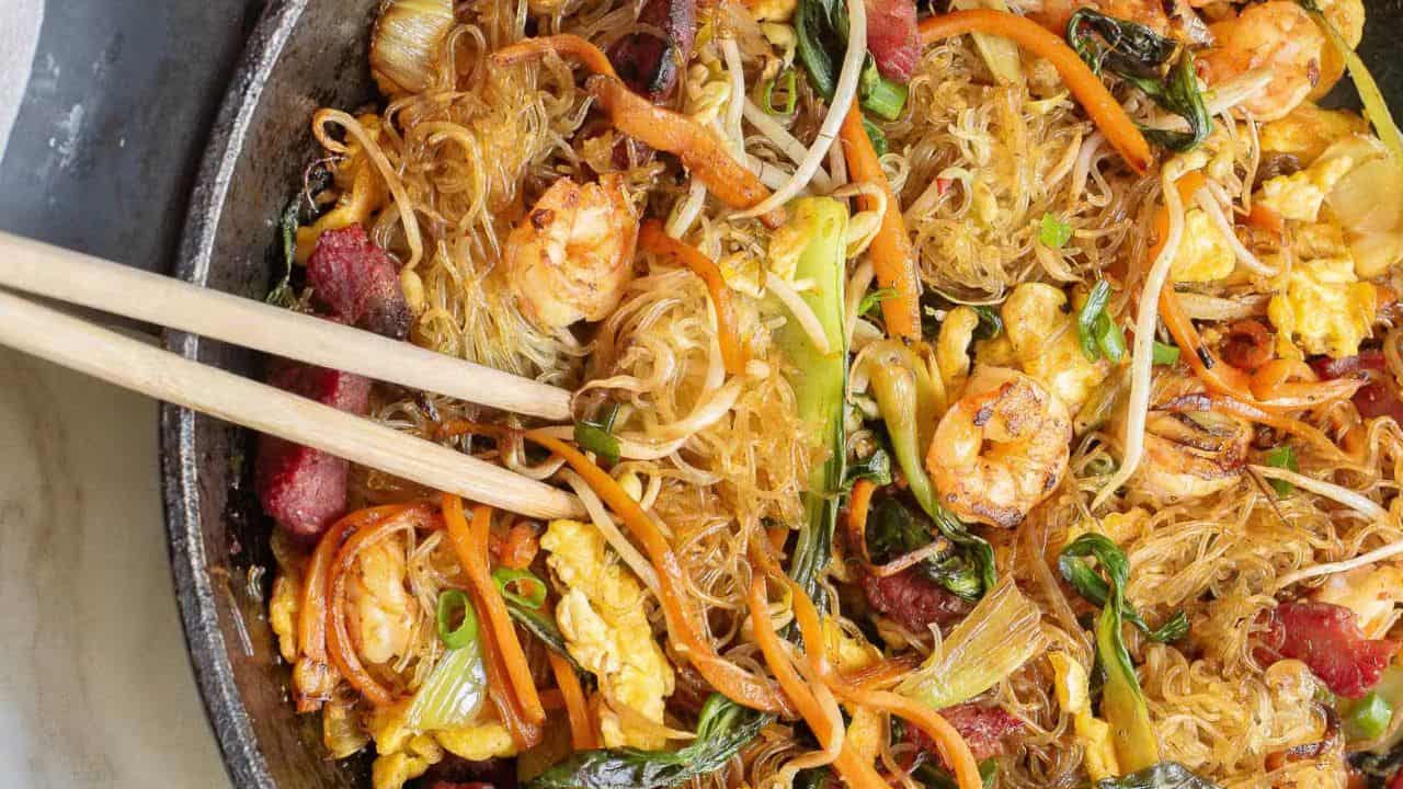 Rice noodles with meat and veggies on a white plate.