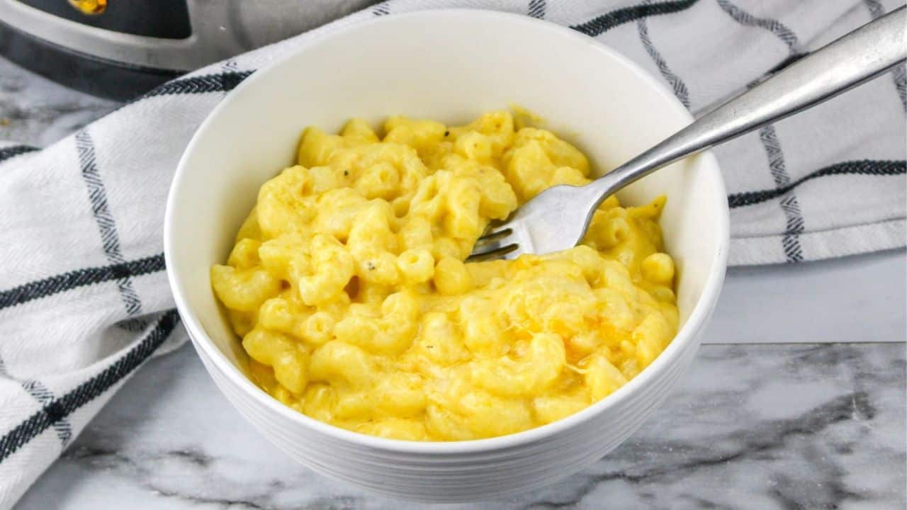 A bowl of creamy macaroni and cheese with a fork, set on a marble surface next to a black and white checkered cloth.
