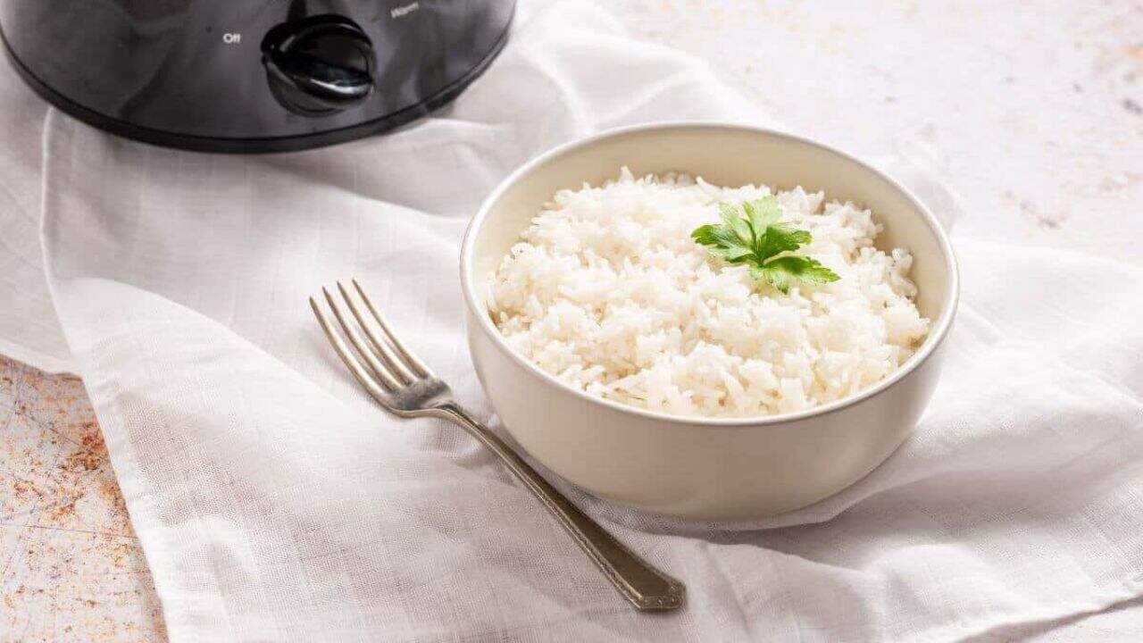 A spoonful of slow-cooked white rice held above a bowl, with a fresh green parsley leaf in the background.