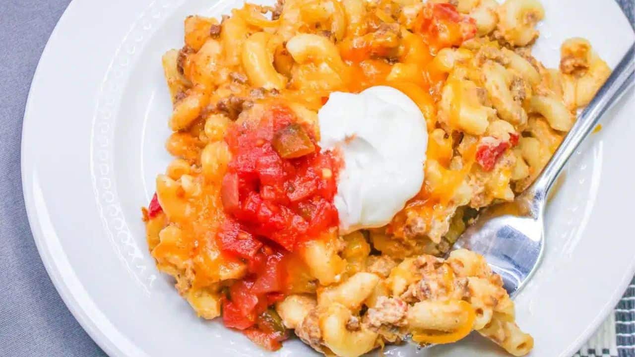 A plate of cheesy pasta with ground meat, topped with tomato sauce and a dollop of sour cream.