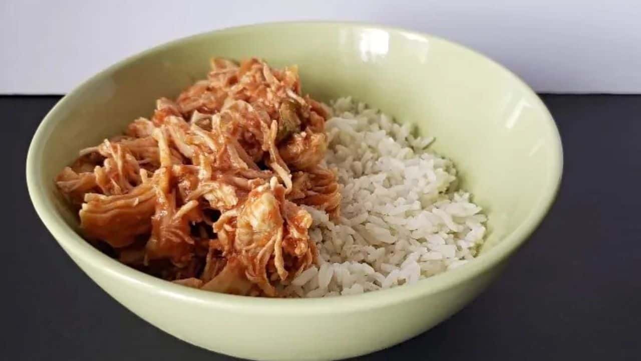 Image shows a Bite of tomato lime chicken on a fork with rice and the rest of the bowl in the background.
