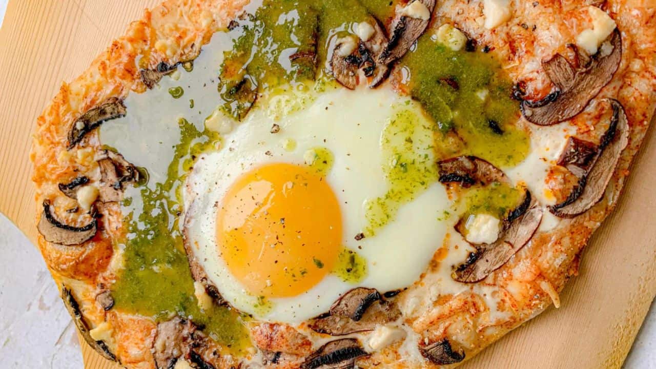Breakfast pizza with mushrooms, green sauce, and egg on wood pizza peel.