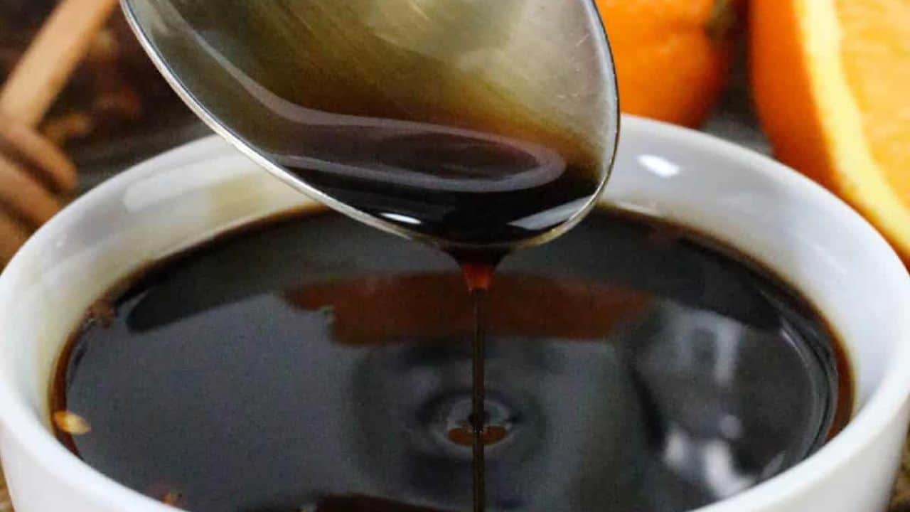 Spoon drizzling rich teriyaki orange sauce into a white bowl.