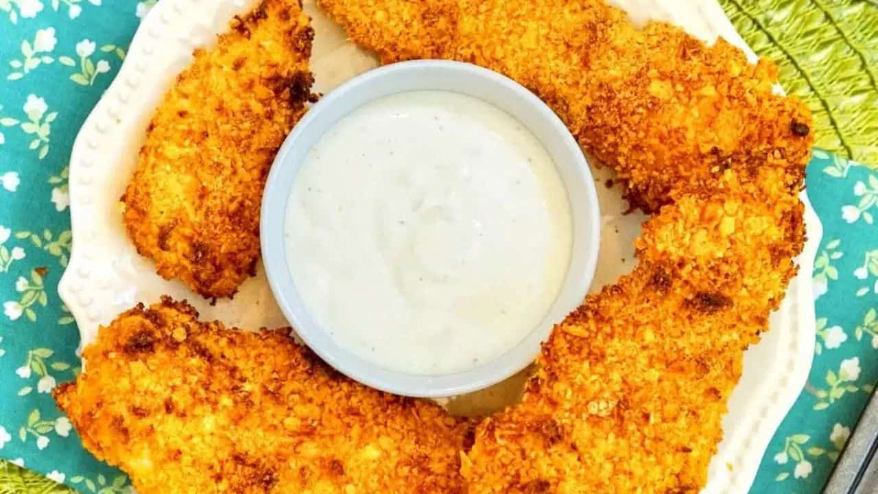A plate of crispy breaded chicken tenders arranged in a circle around a bowl of white dipping sauce.