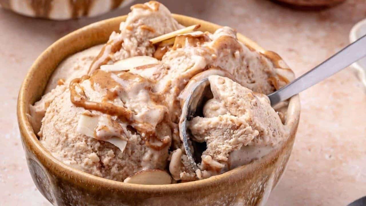 A bowl of creamy ice cream with brown swirls and almond slices, with a spoon scooping out a portion.