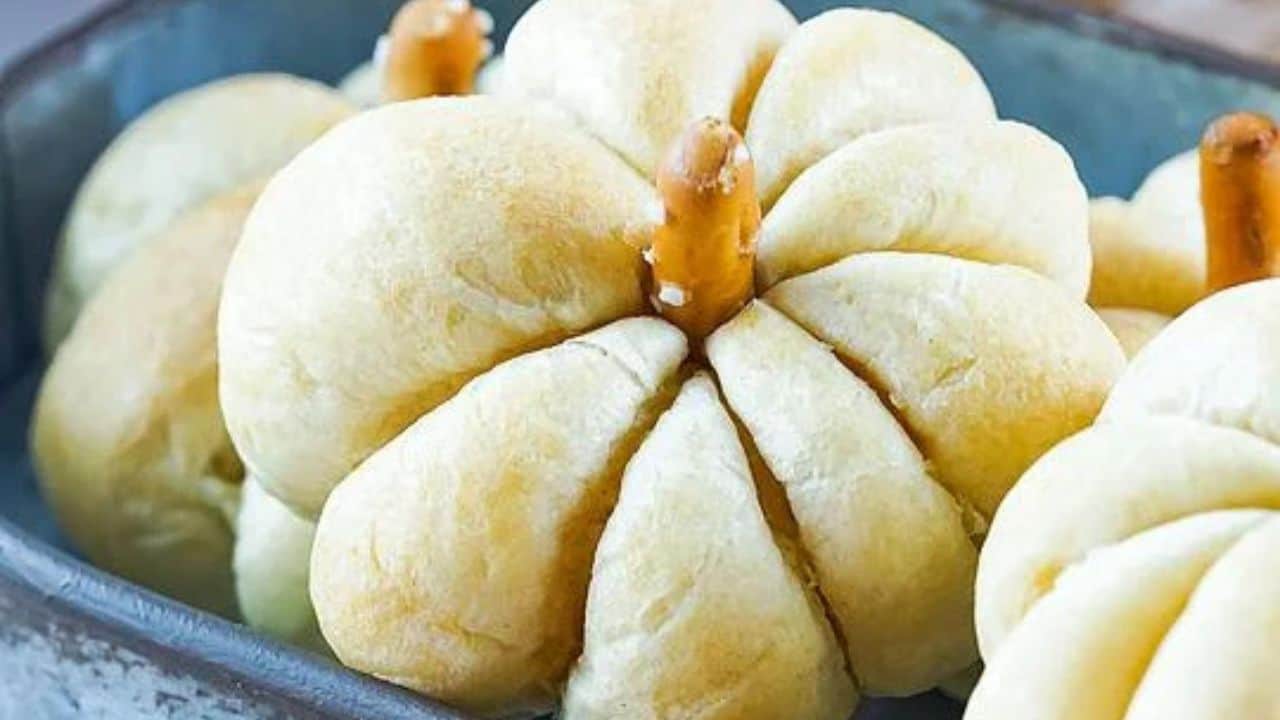 Pumpkin-shaped bread rolls with pretzel sticks as stems arranged in a baking tray.