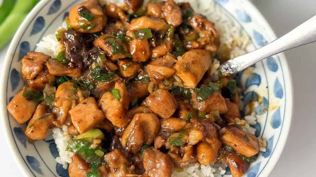A bowl of cooked Chinese scallion chicken served in a white and blue bowl.