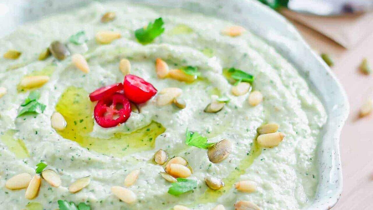 Roasted eggplant dip drizzled with olive oil and topped with pine nuts and parsley in a teal dish.