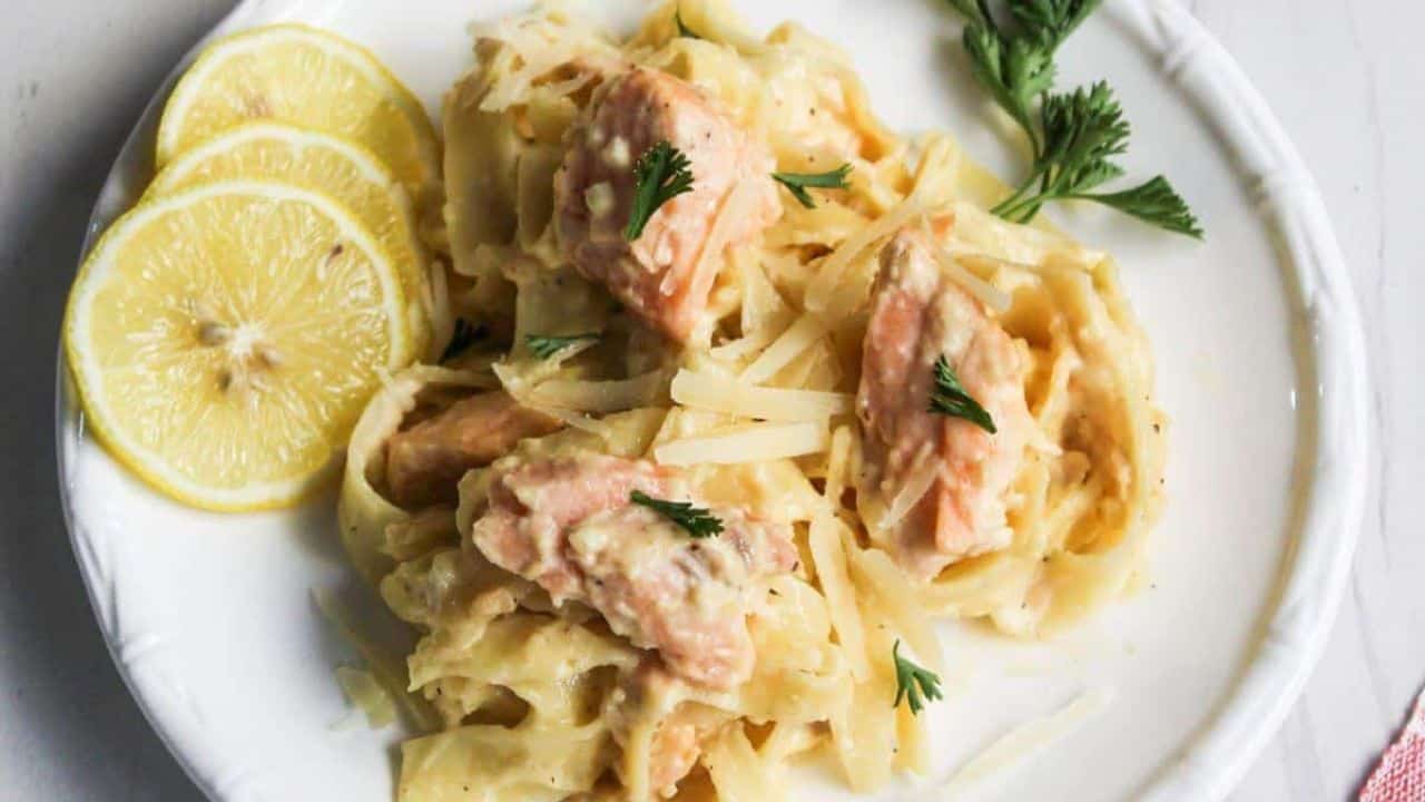 Salmon pasta Alfredo served on a white plate with lemon.