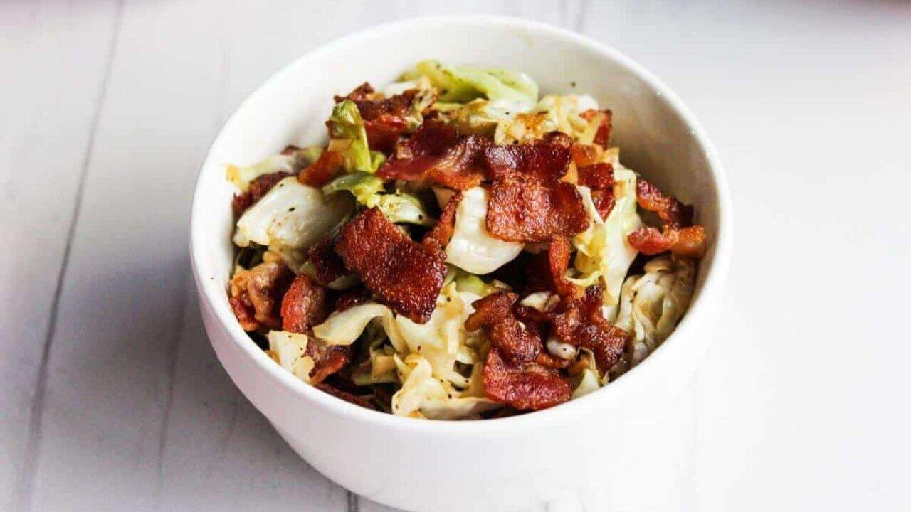 Cabbage and bacon in white serving bowl.
