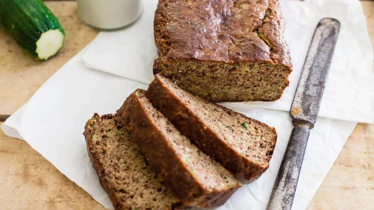 Paleo almond zucchini bread cut into slices with jug of milk, knife and zucchini to the side.
