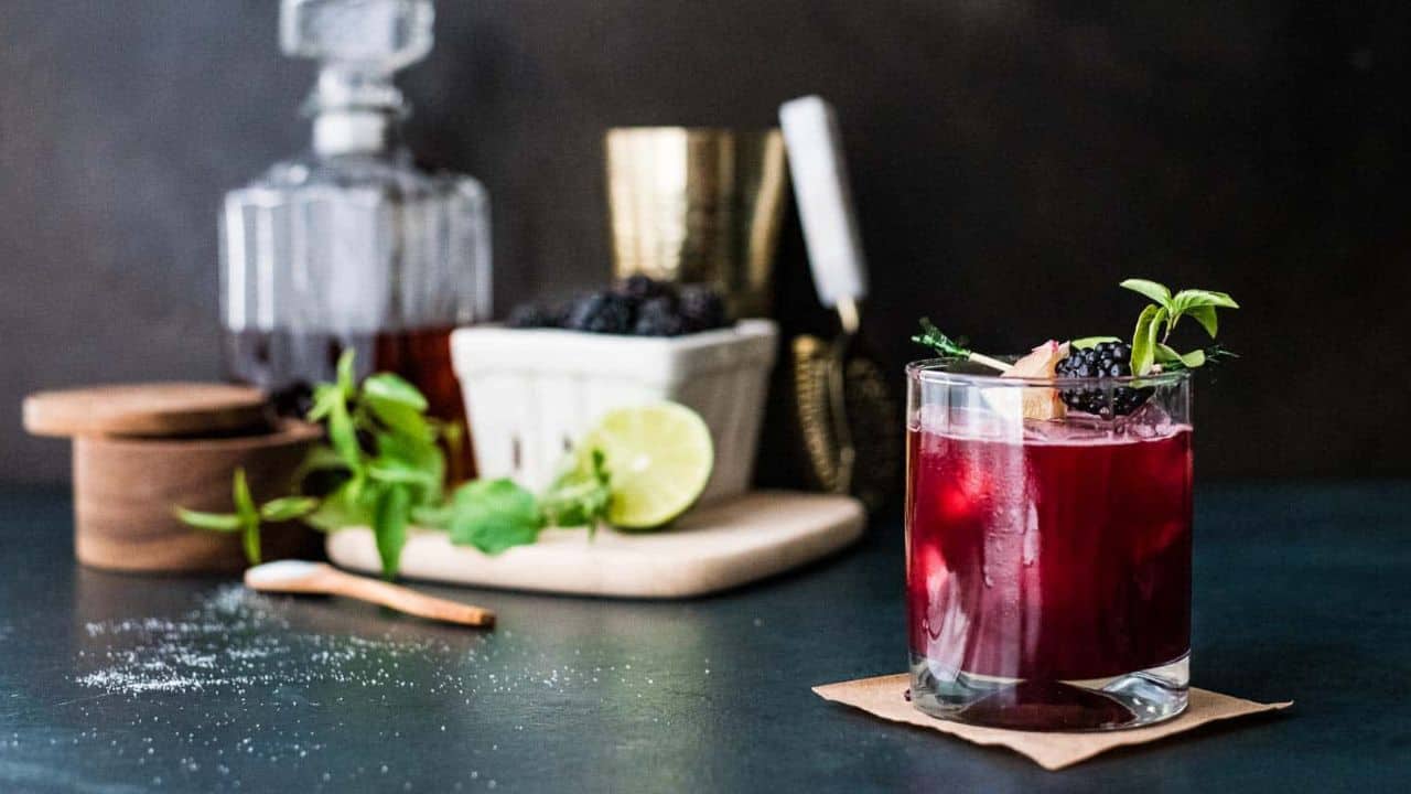 A blackberry bourbon smash in front of a cocktail bar set up.