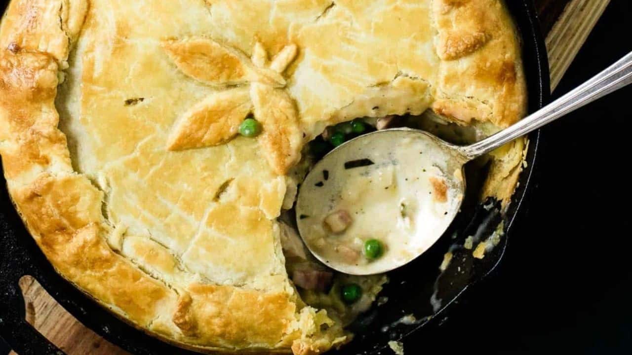 A chicken pot pie in a skillet with a silver spoon rests inside.