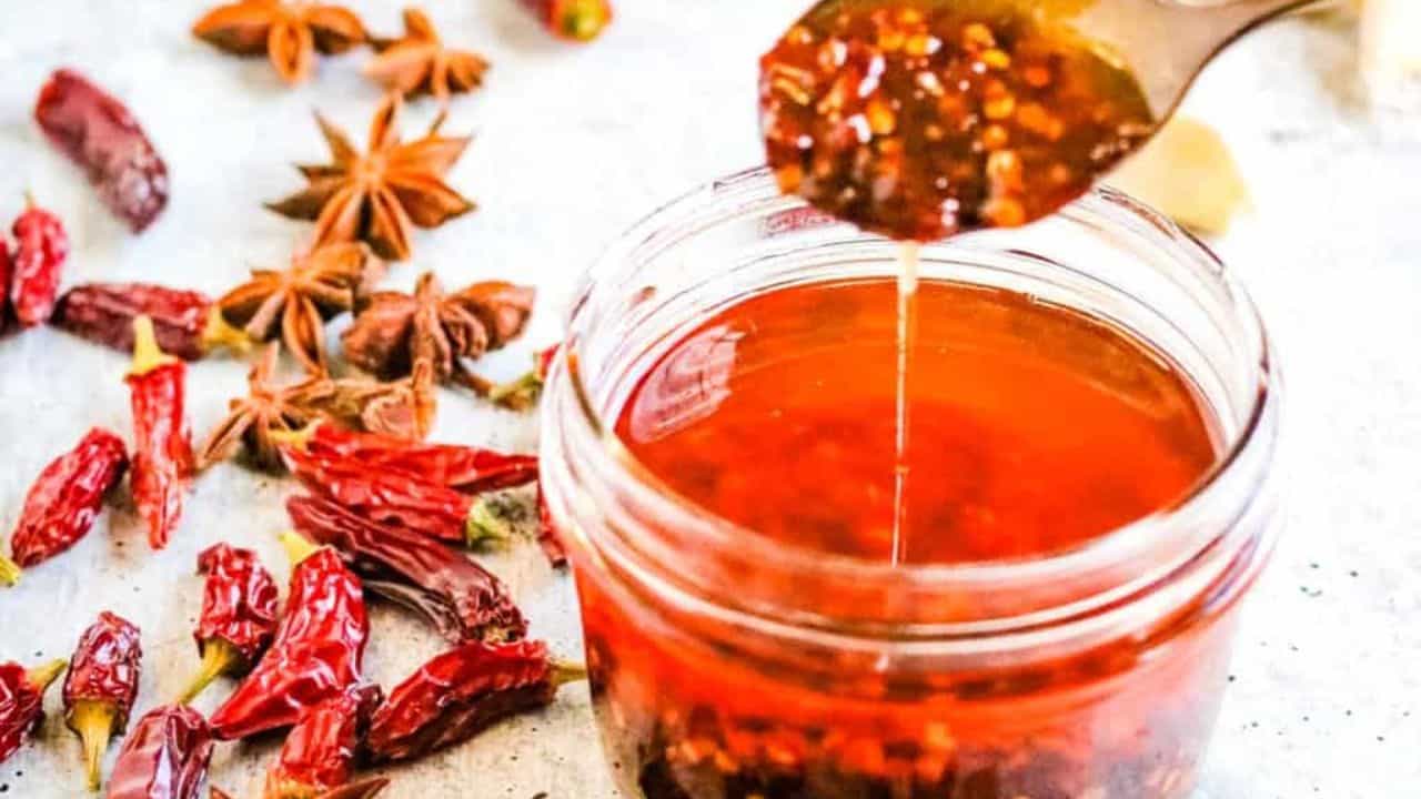 Low angle shot of a jar of chili oil with a spoon lifting some of the oil out of the jar.
