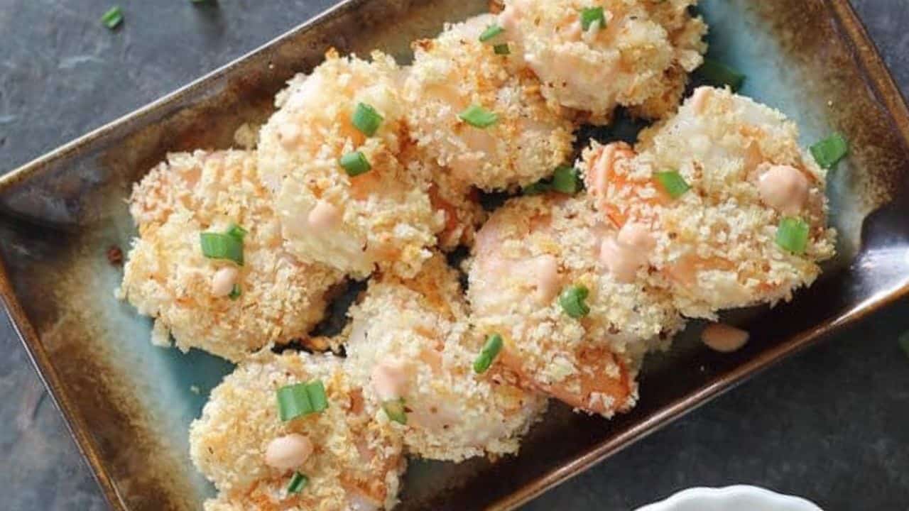 Baked bang bang shrimp on a serving plate garnished with green onions and served with dipping sauce.