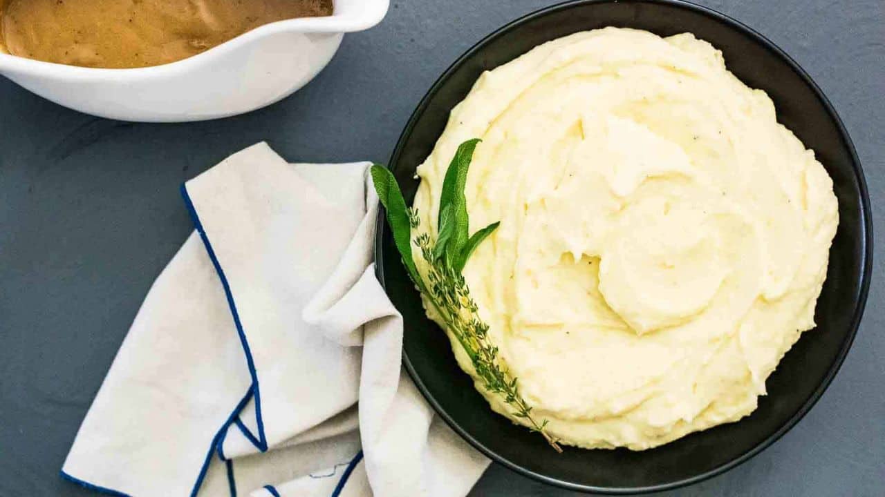 A bowl of mashed potatoes with gravy and sprigs of thyme and sage.