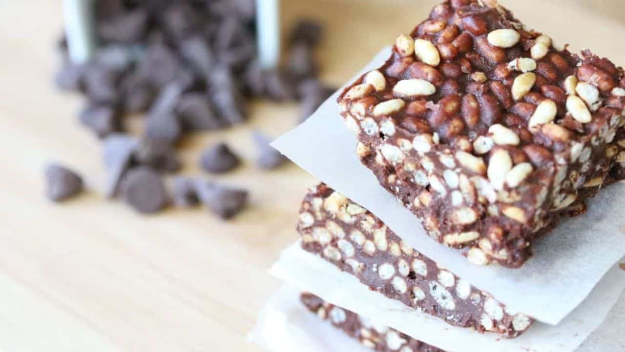 A stack of chocolate rice crispy treats on parchment paper with chocolate chips scattered in the background.