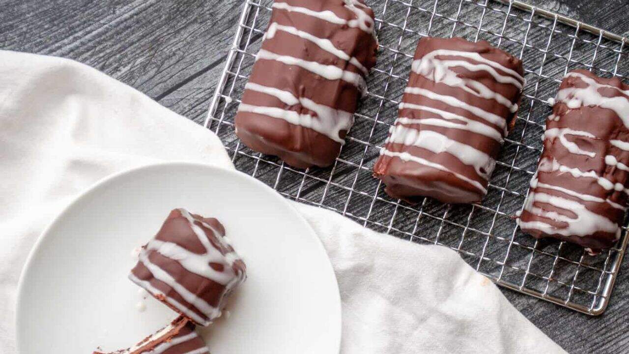 Decadent chocolate mini rolls on a rack and a roll sliced in half on a plate.