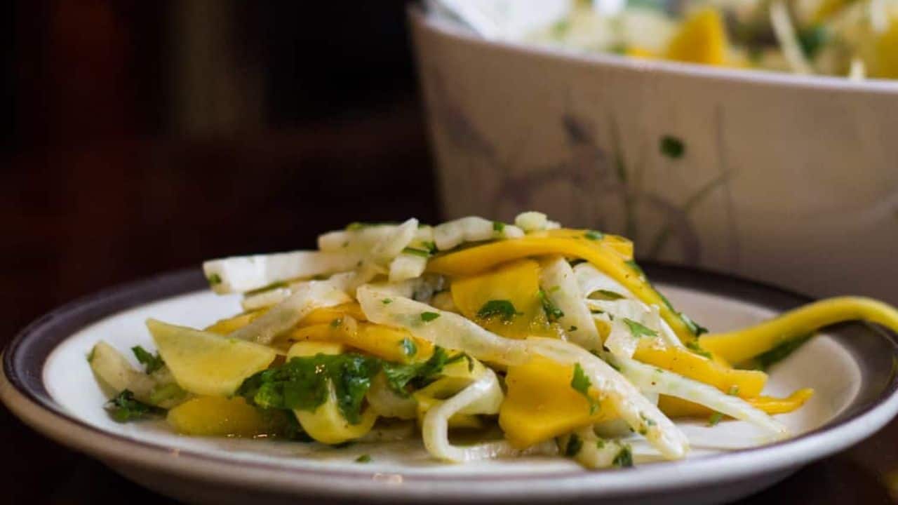 Fennel and mango slaw, featuring thinly sliced mango and shaved fennel, in a white serving dish.
