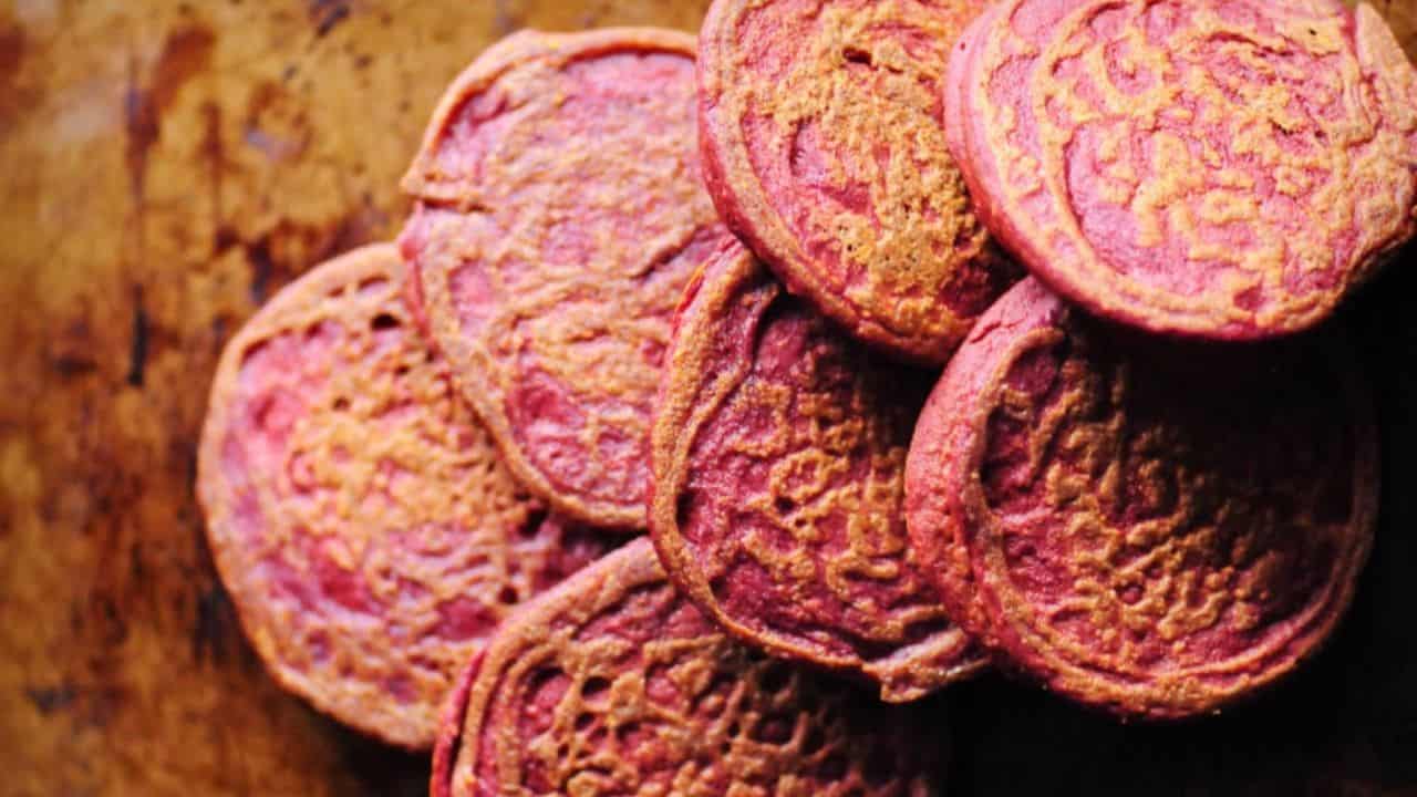 A stack of round, pinkish-orange pancakes sits on a brown surface.