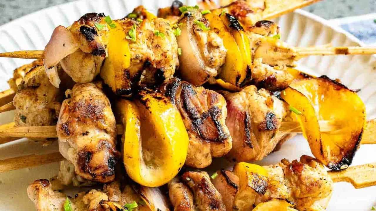 Grilled Greek lemon chicken kabobs with herbs and lemon slices.