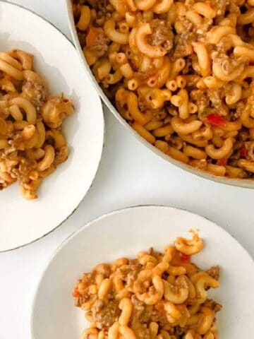 A skillet of macaroni with ground beef and sauce, served on two white plates on a white surface.