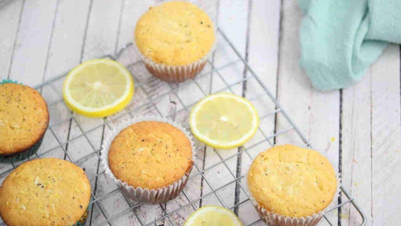 Lemon muffins on a cooling rack with lemon slices, placed on a light wooden surface.