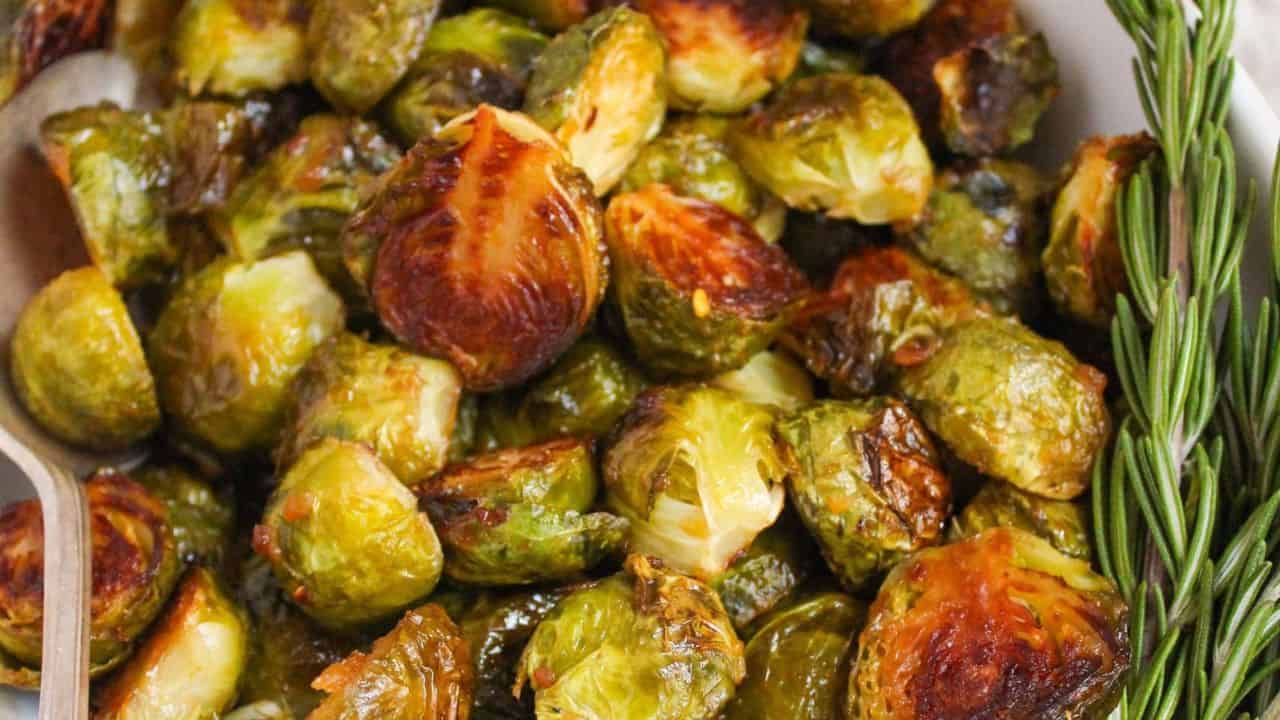 A white serving dish filled with roasted brussels sprouts and fresh rosemary.