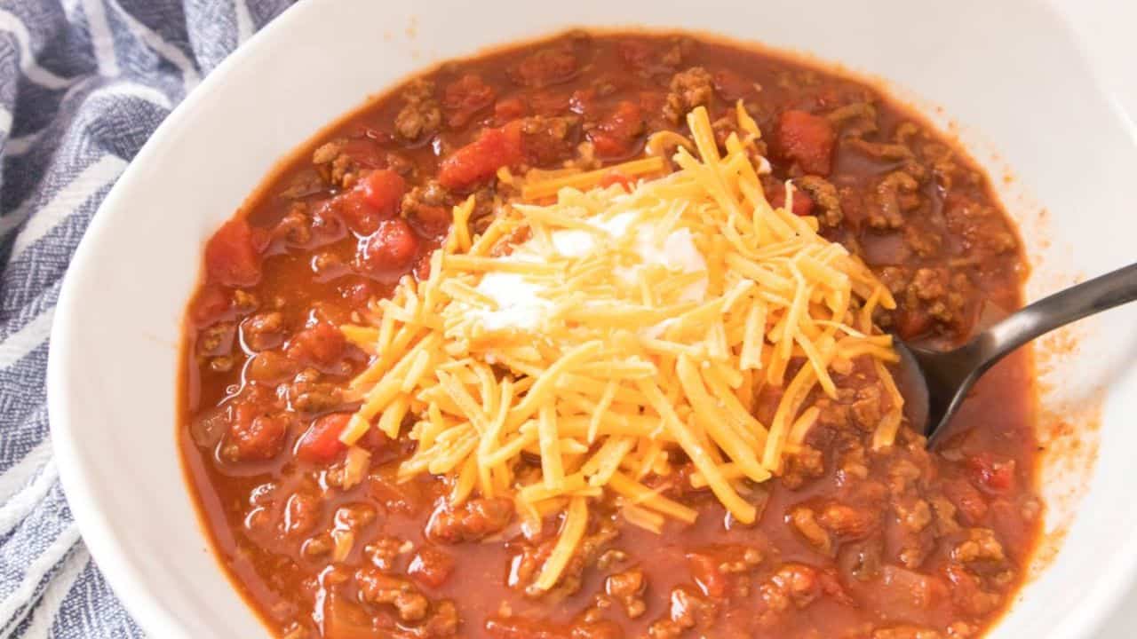 A bowl of chili with shredded cheese in a white bowl.