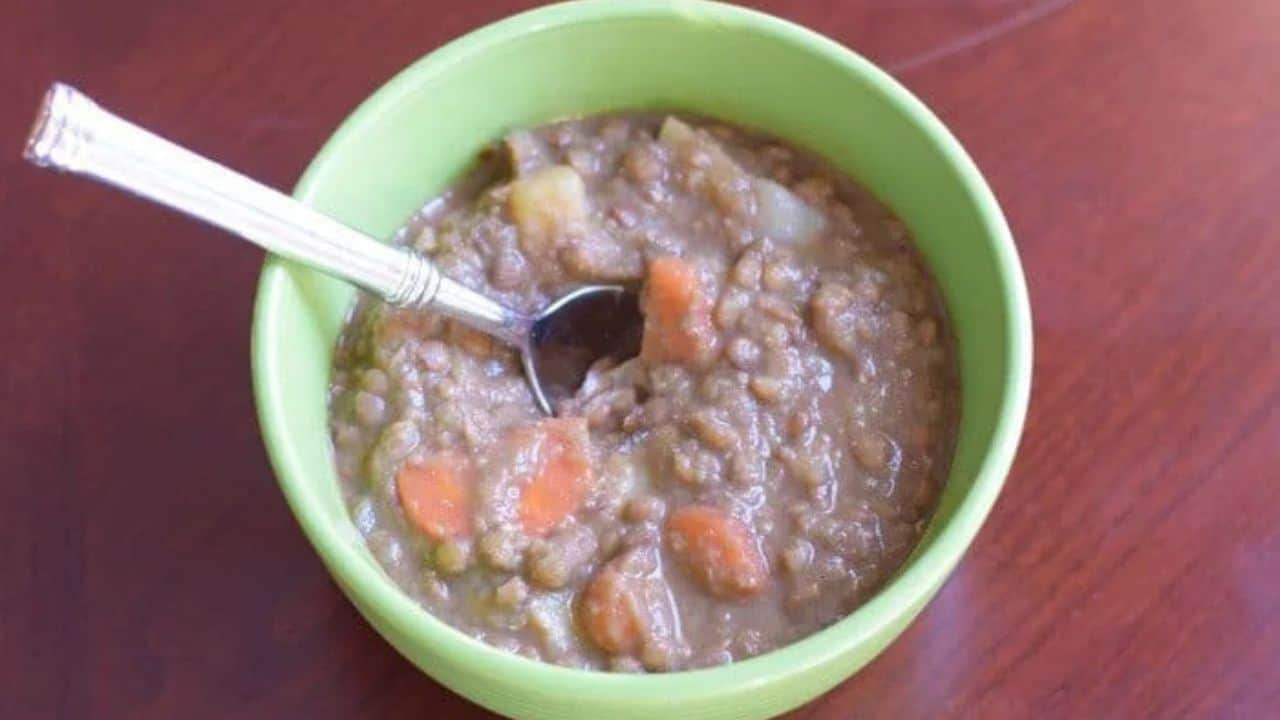 Image shows A bowl of lentil soup with a spoon in it.