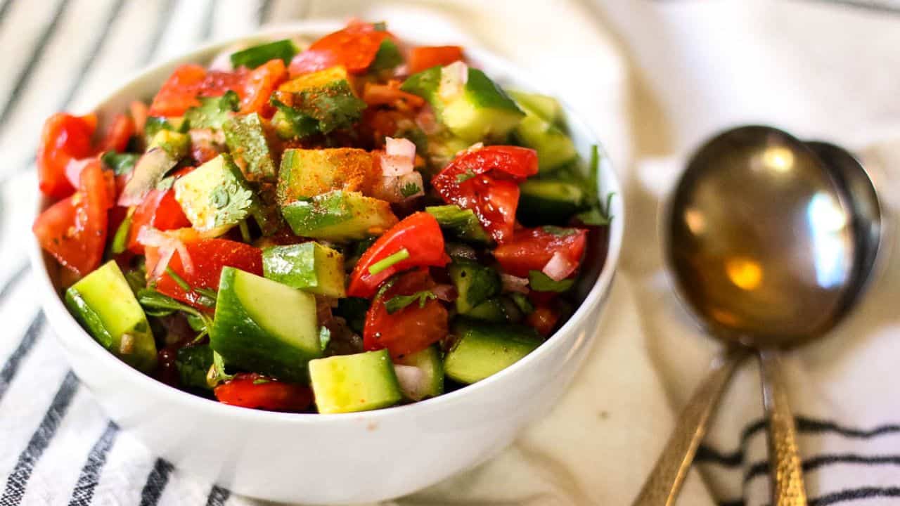 Kachumber salad in a white bowl with fancy silver spoons on the side.