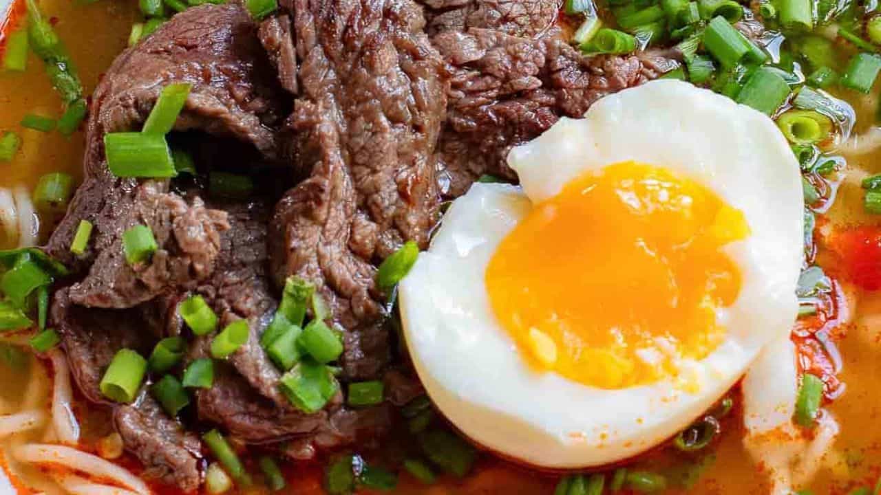 A bowl of beef noodle soup with an egg and chopsticks.