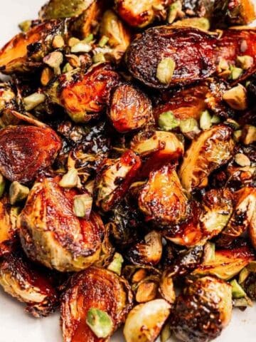 A plate of roasted Brussels sprouts garnished with chopped pistachios, with a small bowl of pistachios on the side.