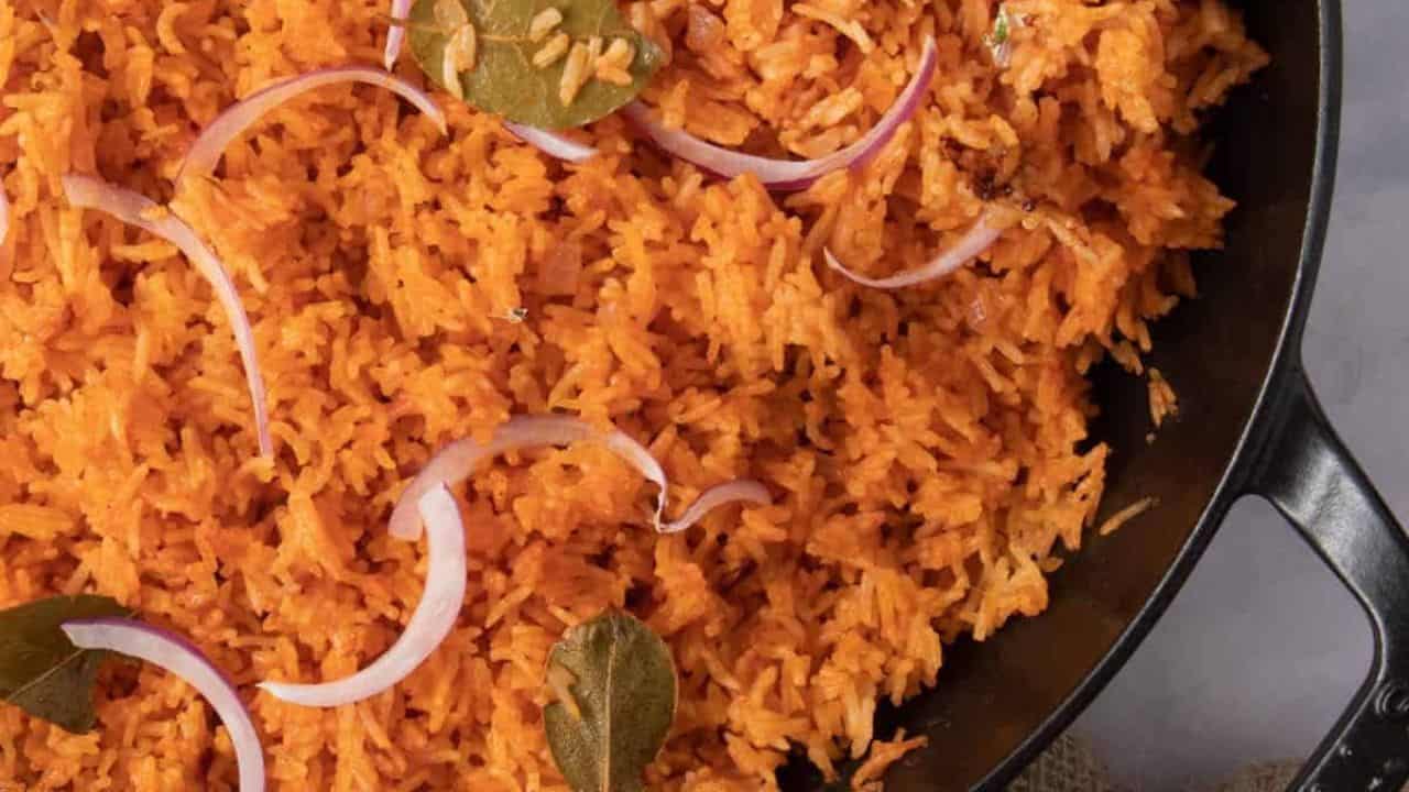 A close up image of nigerian jolloff rice garnished with slices of red onion and bay leaves.
