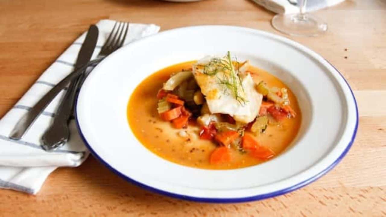 A white plate with a bowl of soup and a glass of wine.