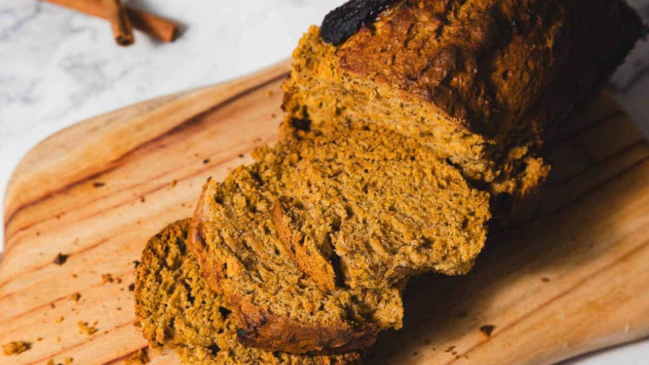 Sliced pumpkin bread on a wooden cutting board next to a glass of milk.