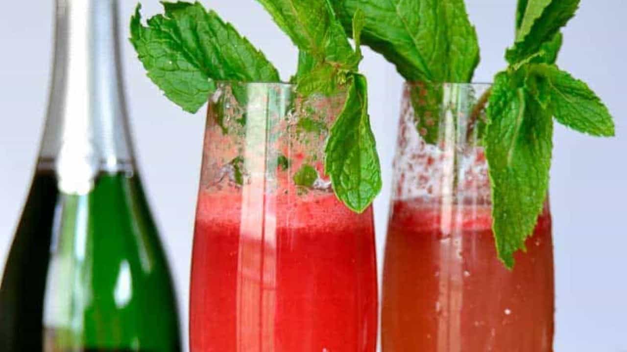 Two champagne flutes filled with a pink mocktail garnished with mint leaves. A bottle labeled