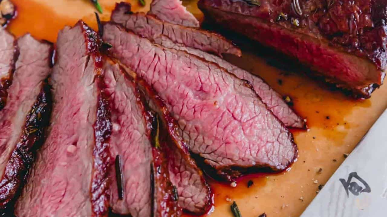 Reverse seared tri tip cut in half on a cutting board with fresh rosemary.