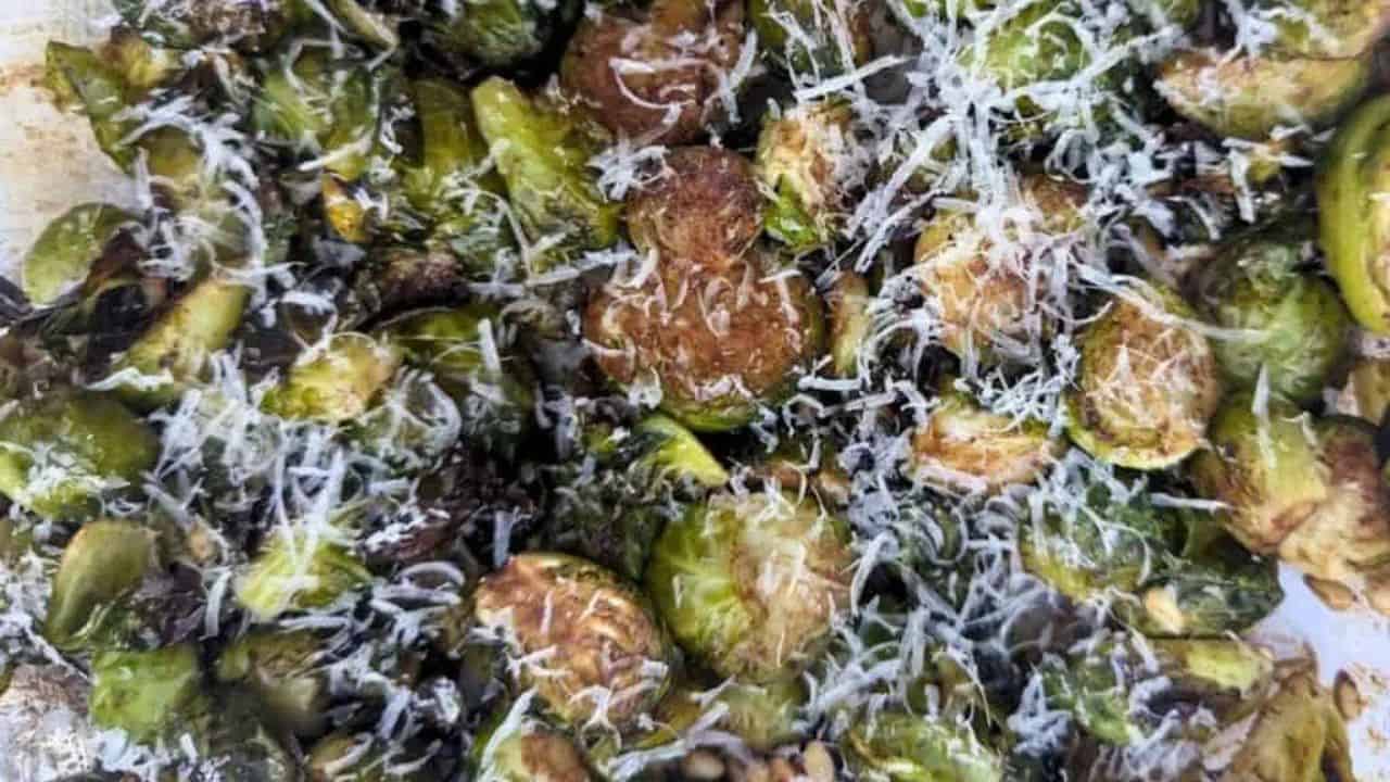 Image shows sliced roasted Brussels sprouts topped with grated Parmesan cheese.