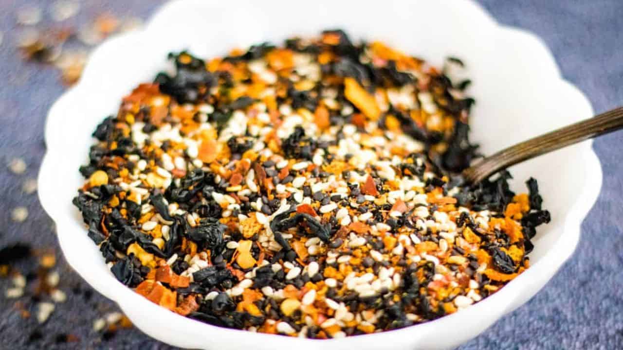Low angle shot of a white bowl filled with shichimi togarashi with a spoon in it.