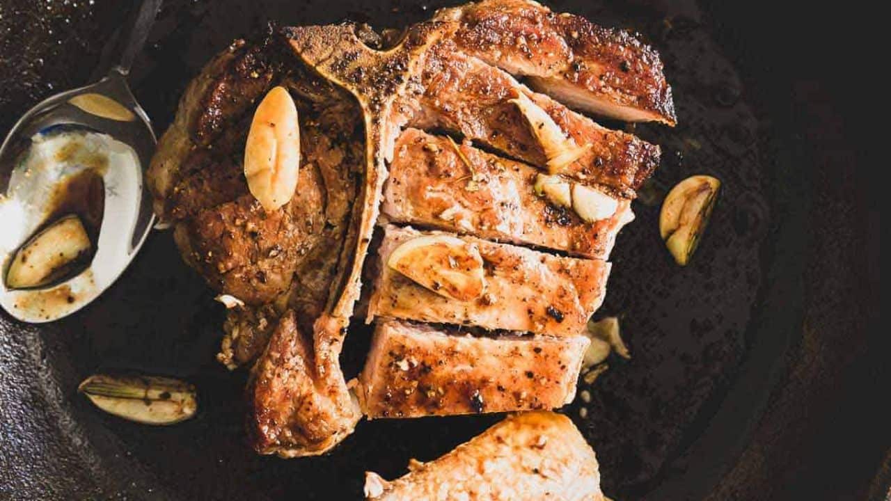 Bone in pork chop sliced in a skillet with garlic cloves.