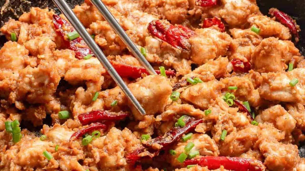 Stir-fried diced chicken with dried chilies and spring onions in a black skillet.