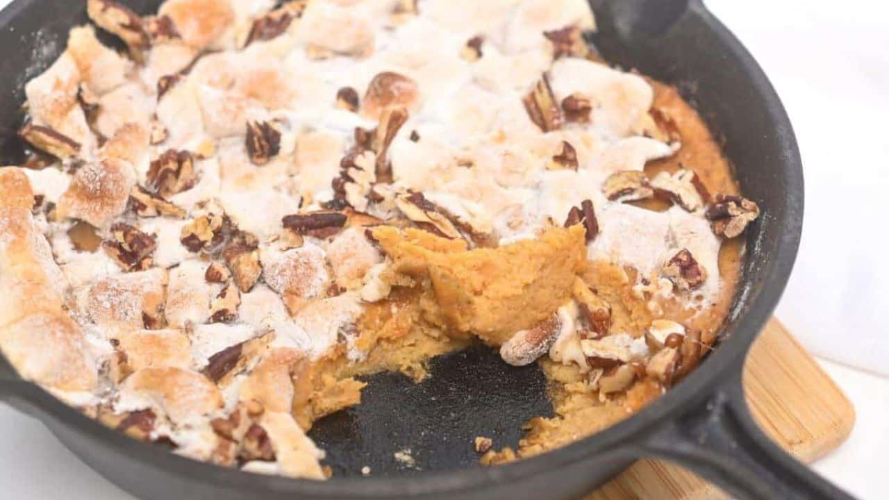 Close-up of a spoonful of sweet potato casserole with a topping of toasted pecans and marshmallows.