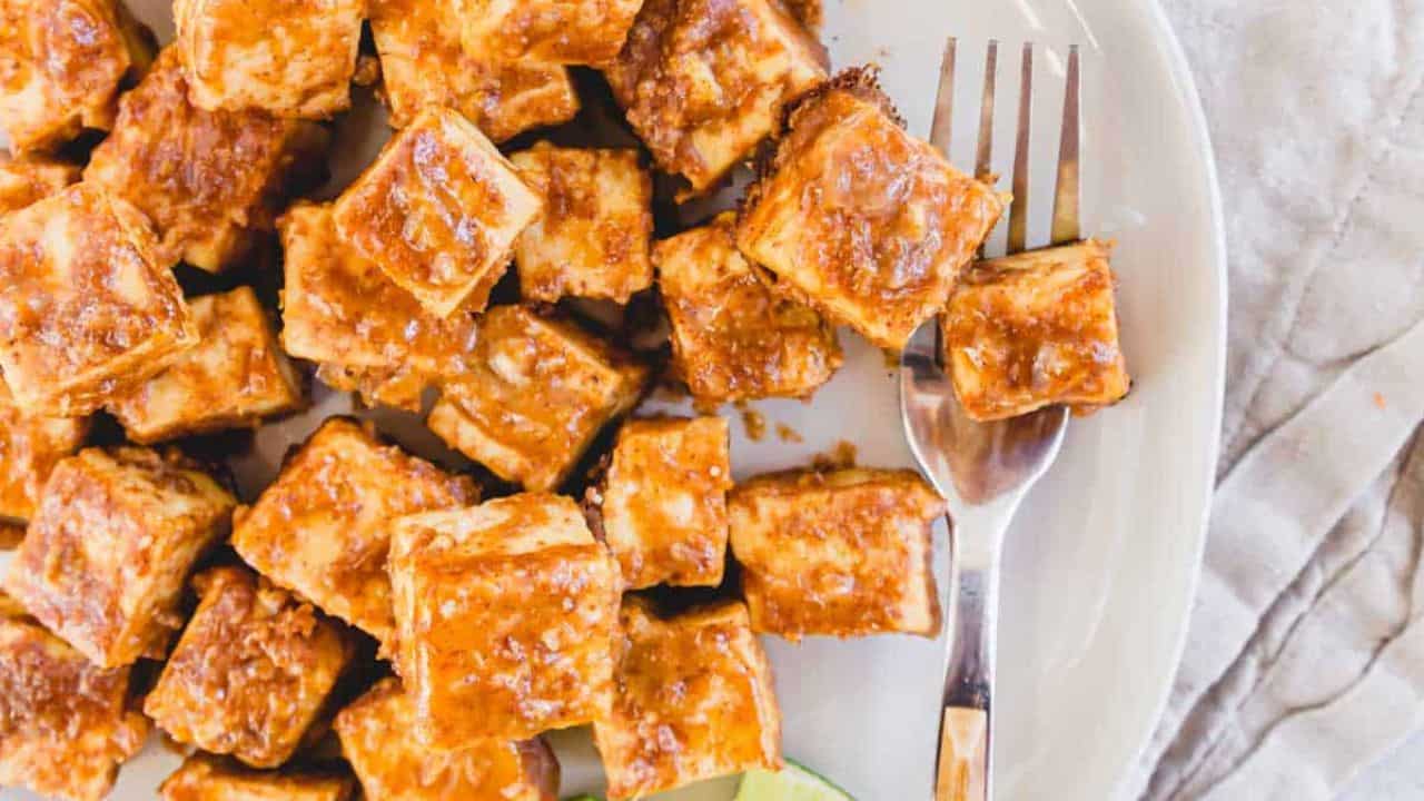 Tofu on a plate with lime wedges and a fork.